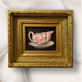 Decorative gold frame with a painting of a teacup and saucer on a white background