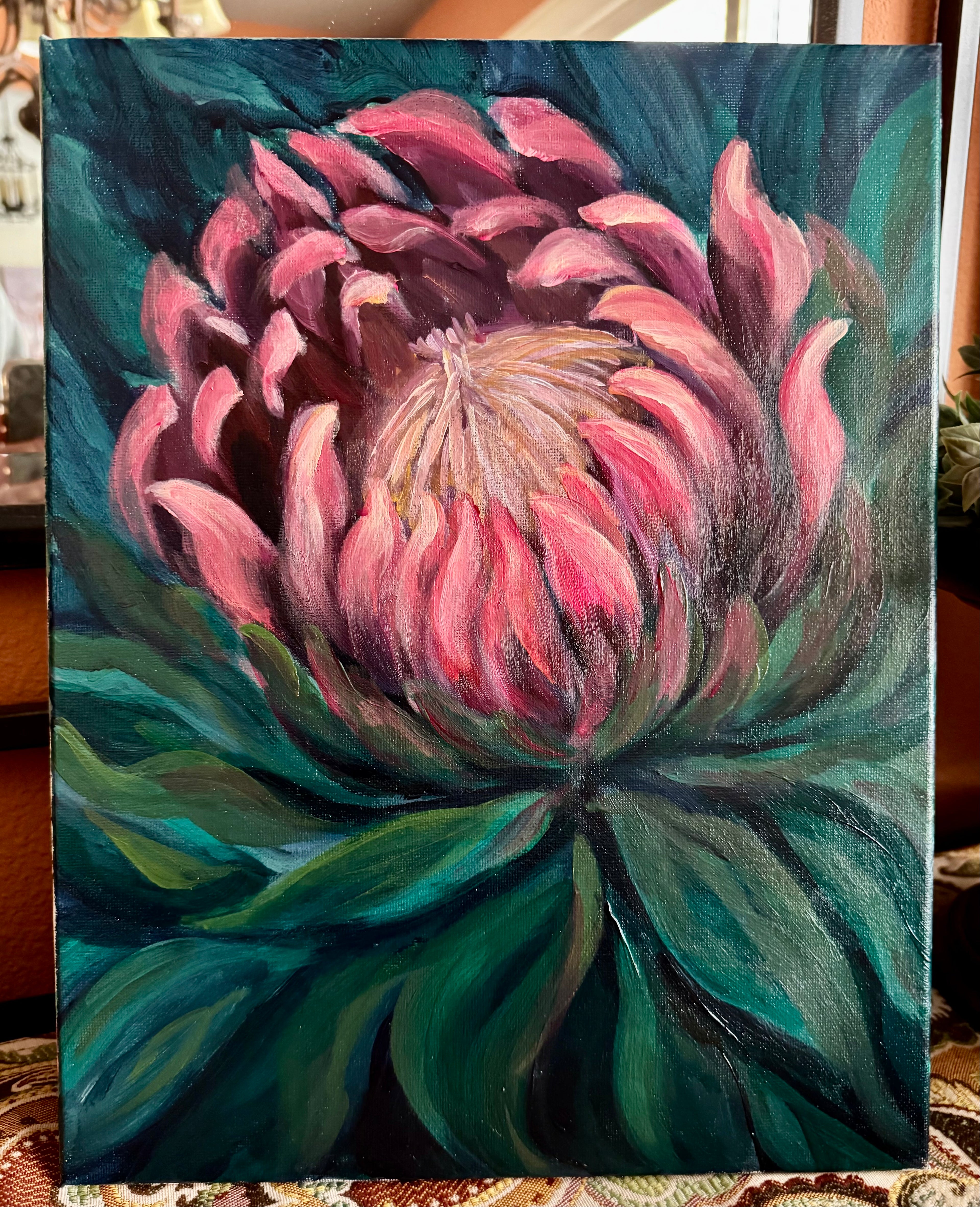Painting of a pink protea flower with green leaves on a textured surface