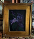 Framed lilac still life painting with purple blooms emerging from dark background