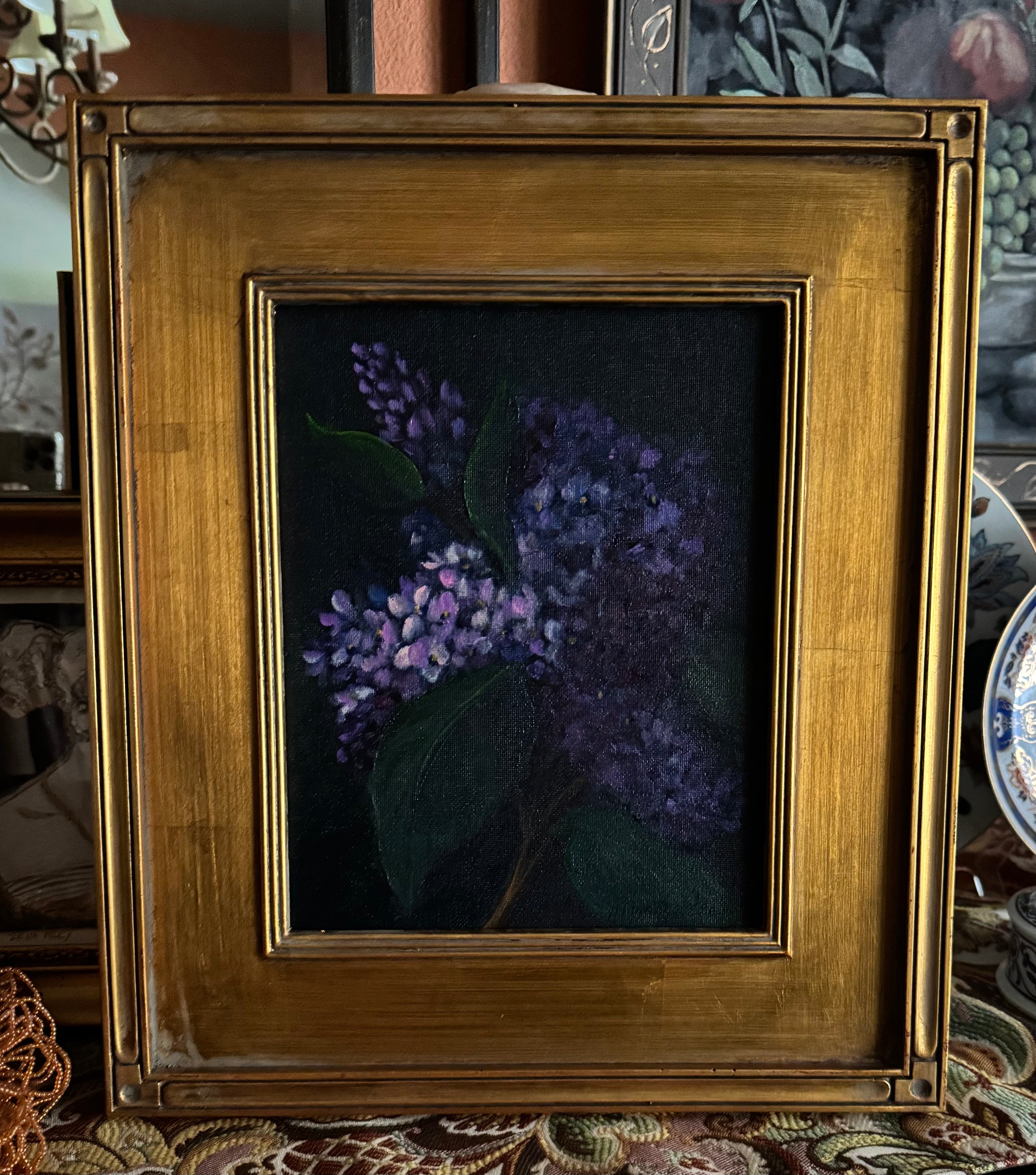 Framed lilac still life painting with purple blooms emerging from dark background