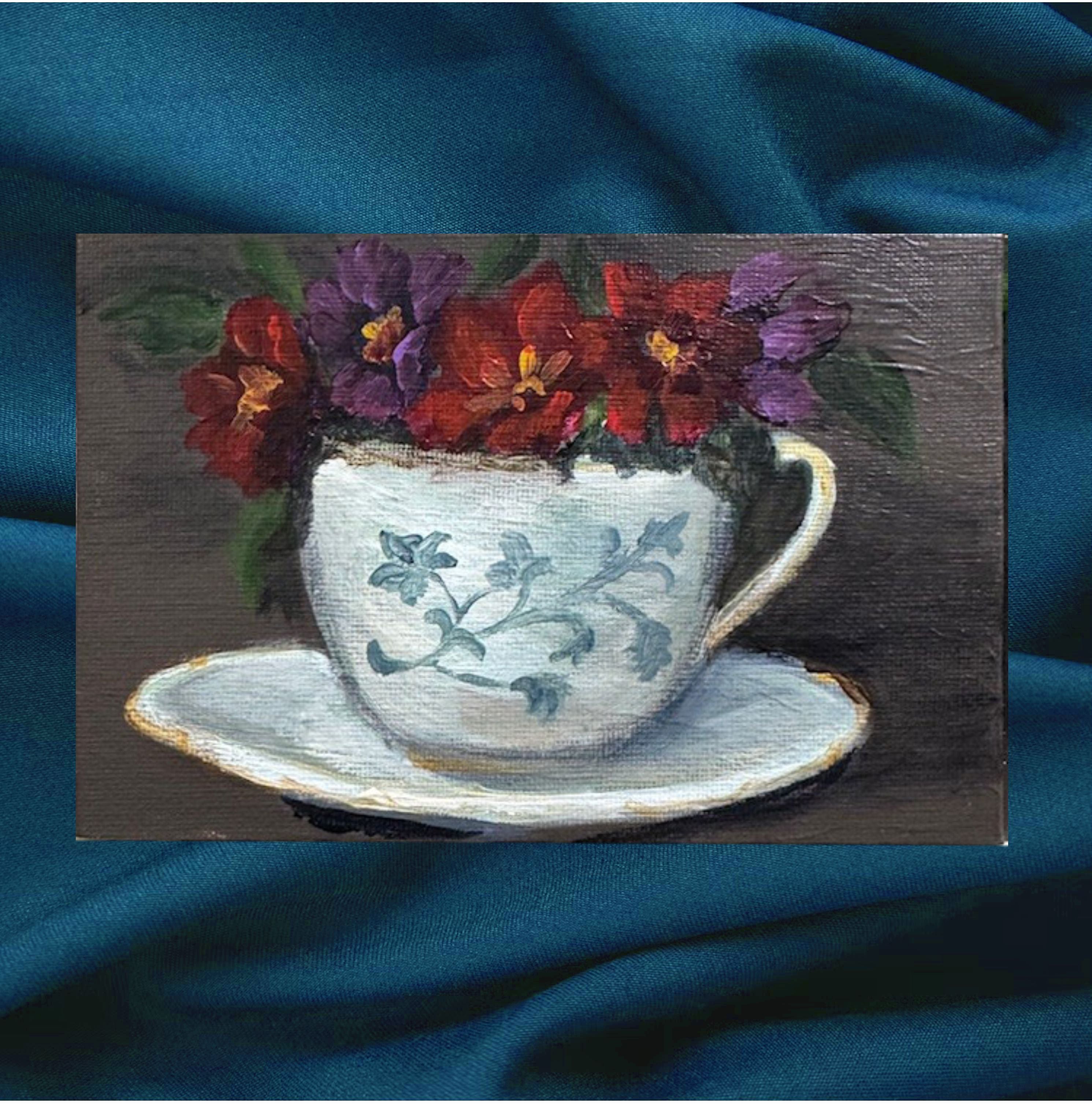 Painting of a teacup with flowers on a blue fabric background